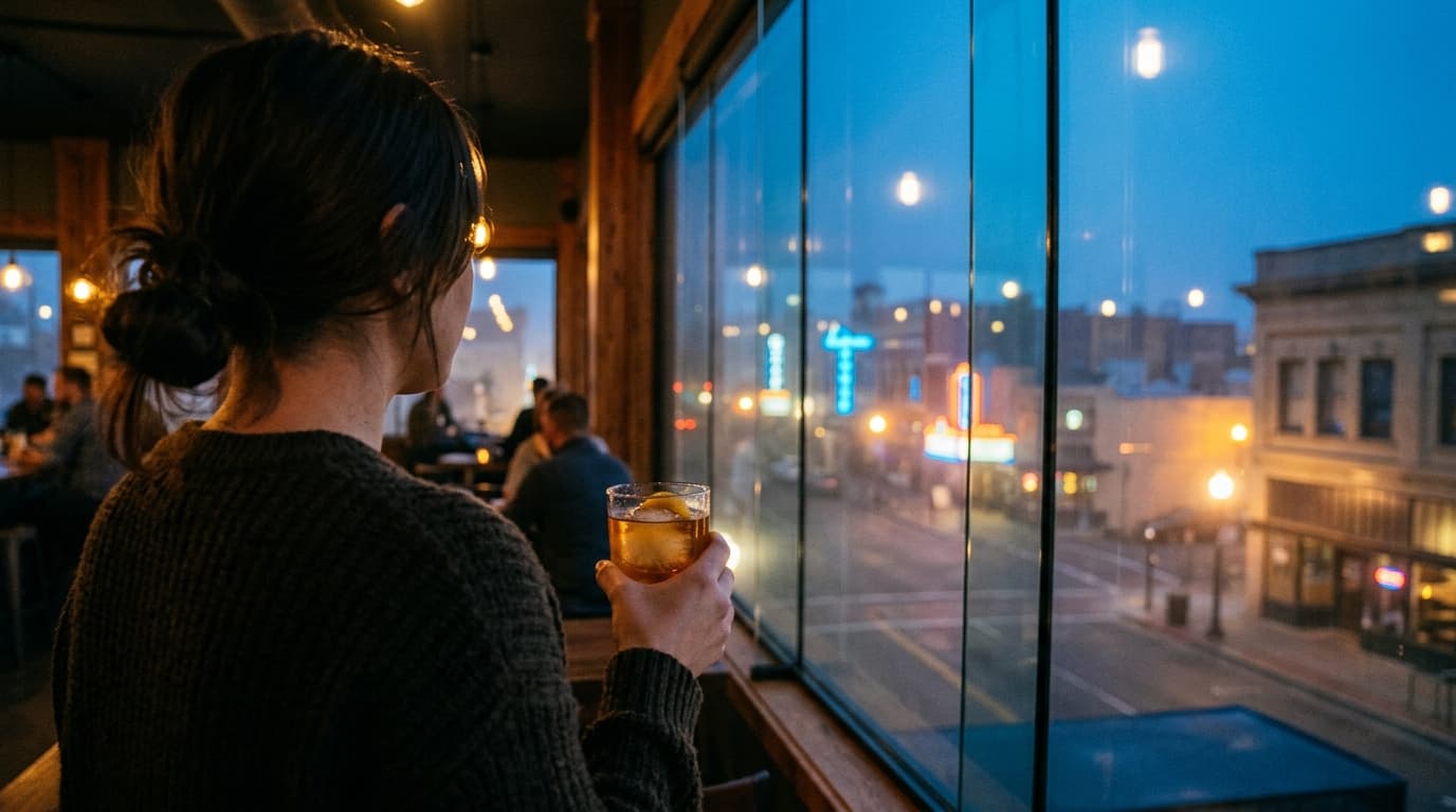 An over-the-shoulder view captures a person holding a craft cocktail at Modernist, their blurred silhouette offset left. B...