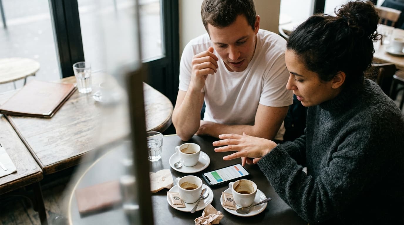 Overhead flat-lay, 35mm documentary, overcast morning. A woman in a charcoal sweater and a man in a white tee sit offset r...